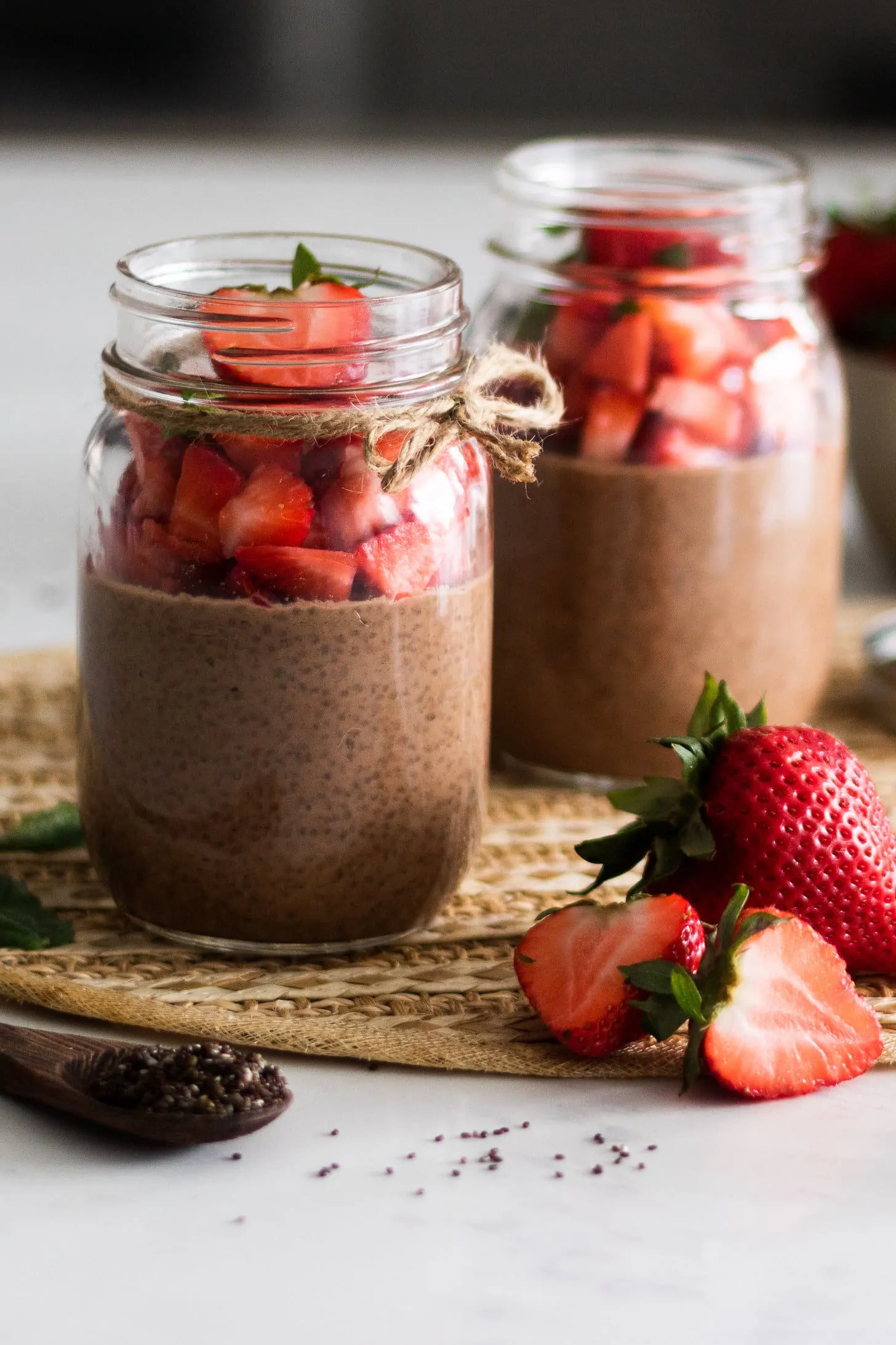 mason jars of chocolate chia pudding topped with chopped strawberries - on different planes.