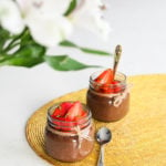 two mini mason jars of chocolate chia pudding topped with chopped strawberries