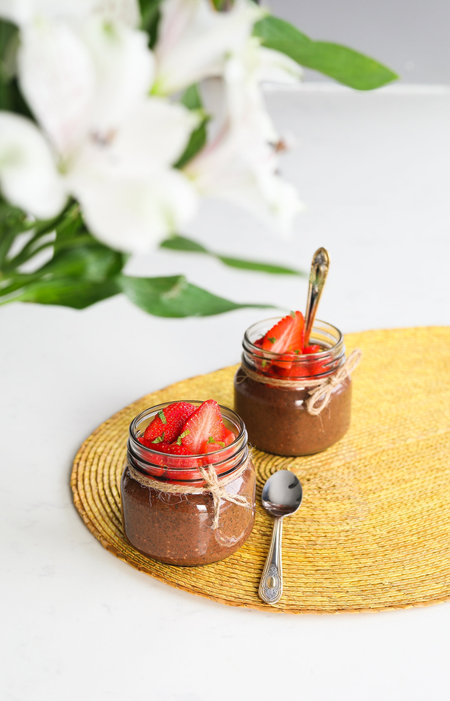 two mini mason jars of chocolate chia pudding topped with chopped strawberries