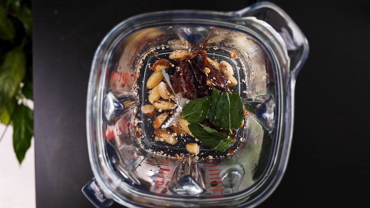 birds eye view of the inside of a blender with brazil nuts, water, dates and mint.