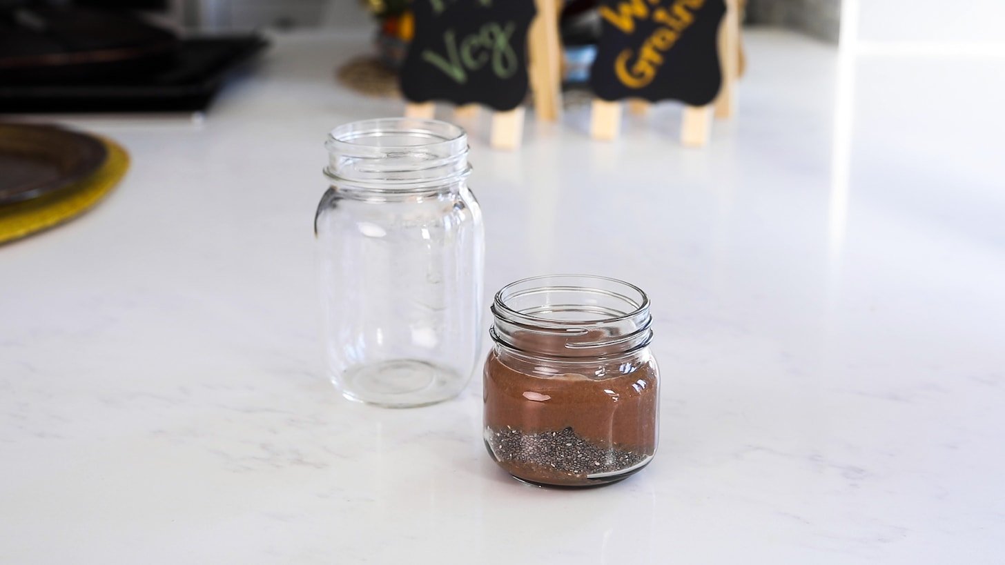 two mason jars: a small one filled with chia seeds and chocolate milk and the other one is empty.