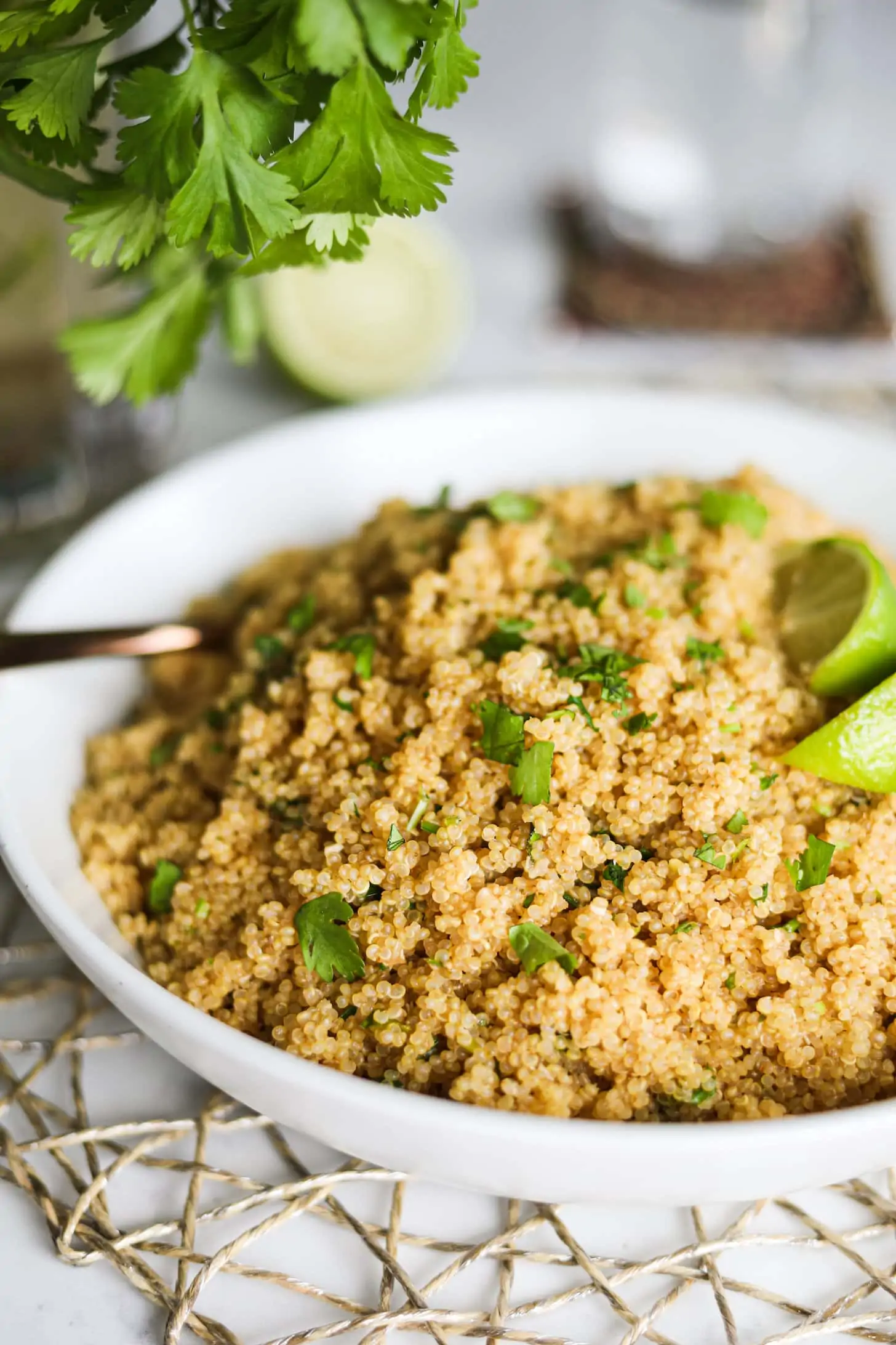 perspective shot of a bowl of cooked quinoa topped with lime wedges with some herbs hanging over the top.