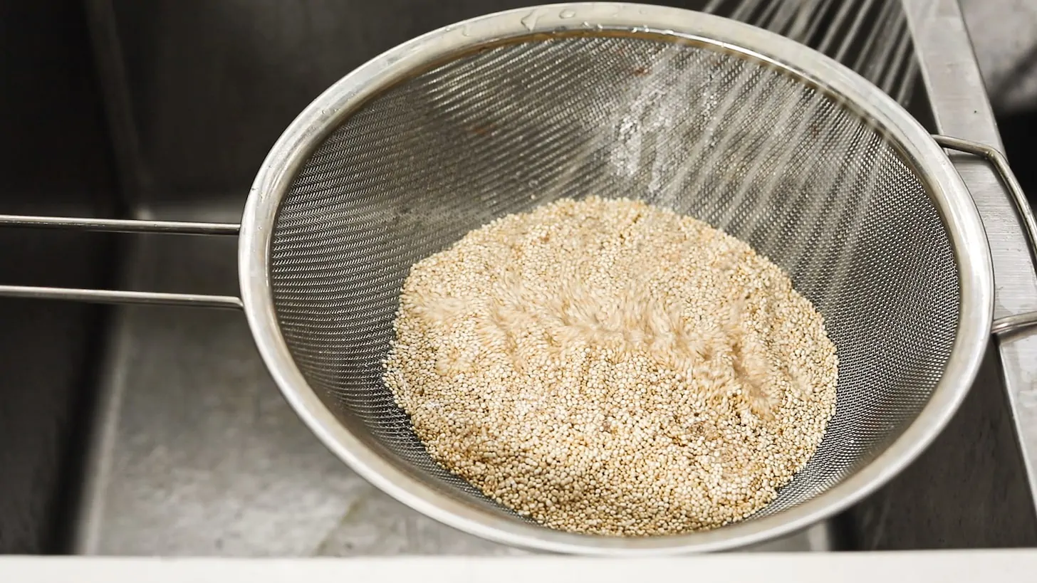 a sieve of quinoa with water splashing over it in a sink.