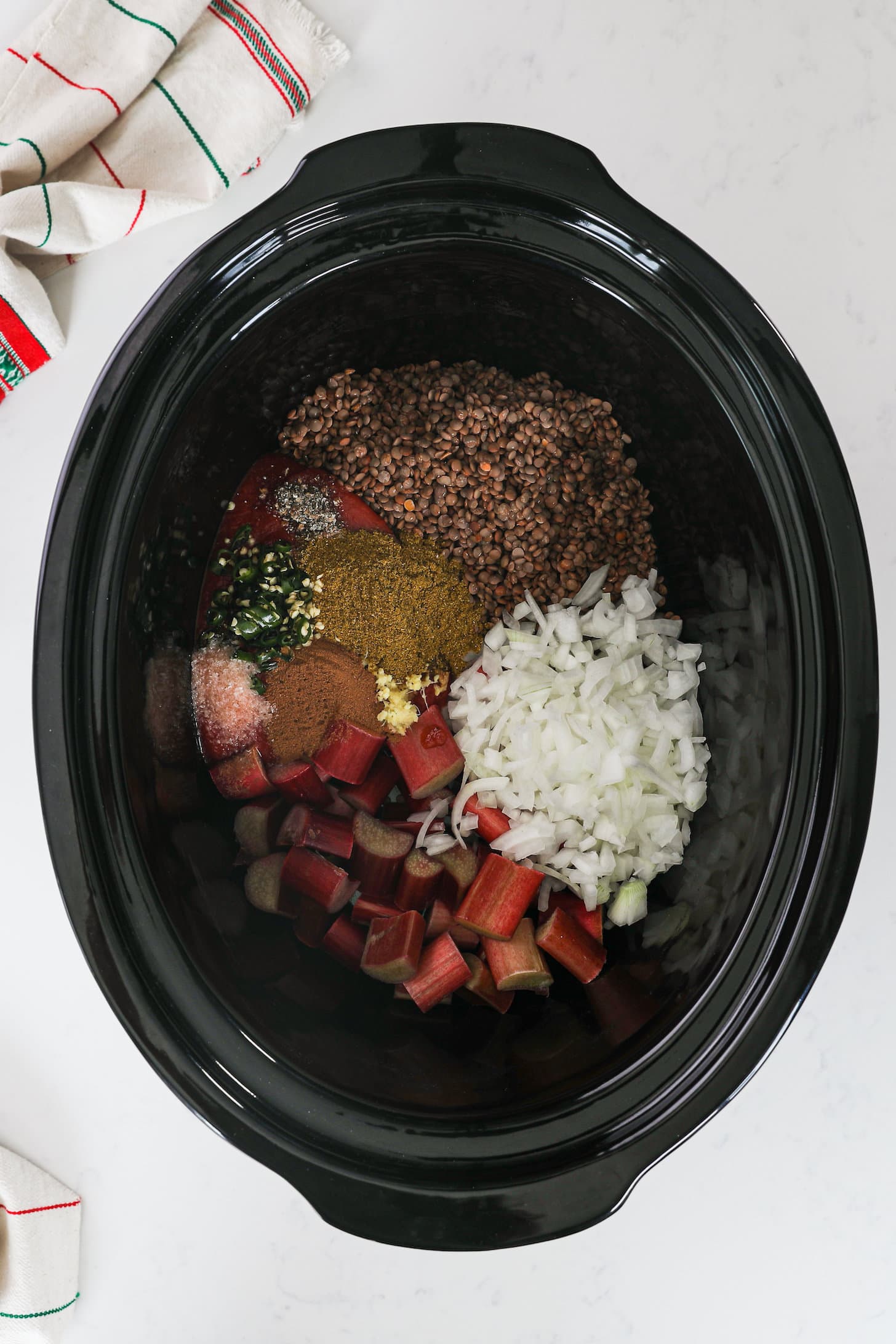 overhead shot of a black clay pot with ingredients arranged in it, featuring lentils, onion, rhubarb and spices.