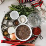 overhead shot of a collection of food ingredients styled in a silver round tray with a red and cream traditional scarf on one side.