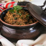 angled shot of a round clay container with cooked lentils in a tray styled with a cream coloured scarf.