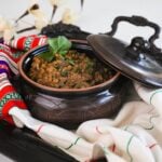 angled shot of a round clay container with cooked lentils in a tray styled with a cream coloured scarf.