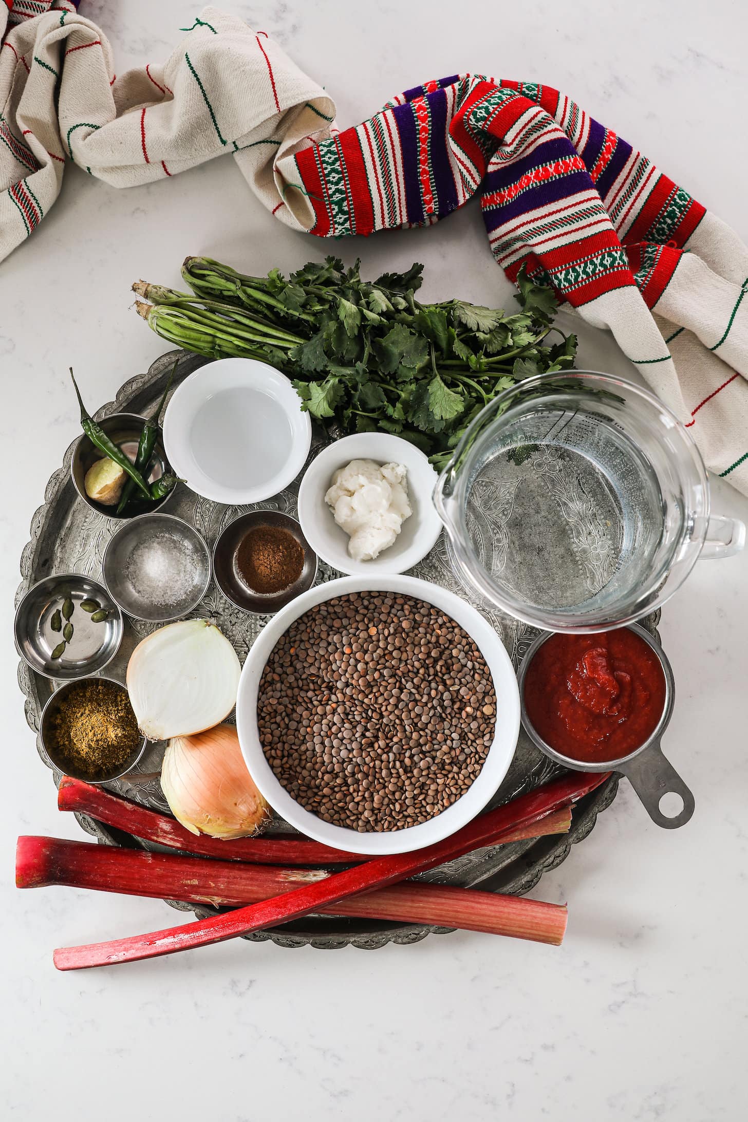 overhead shot of a collection of food ingredients styled in a silver round tray with a red and cream traditional scarf on one side.