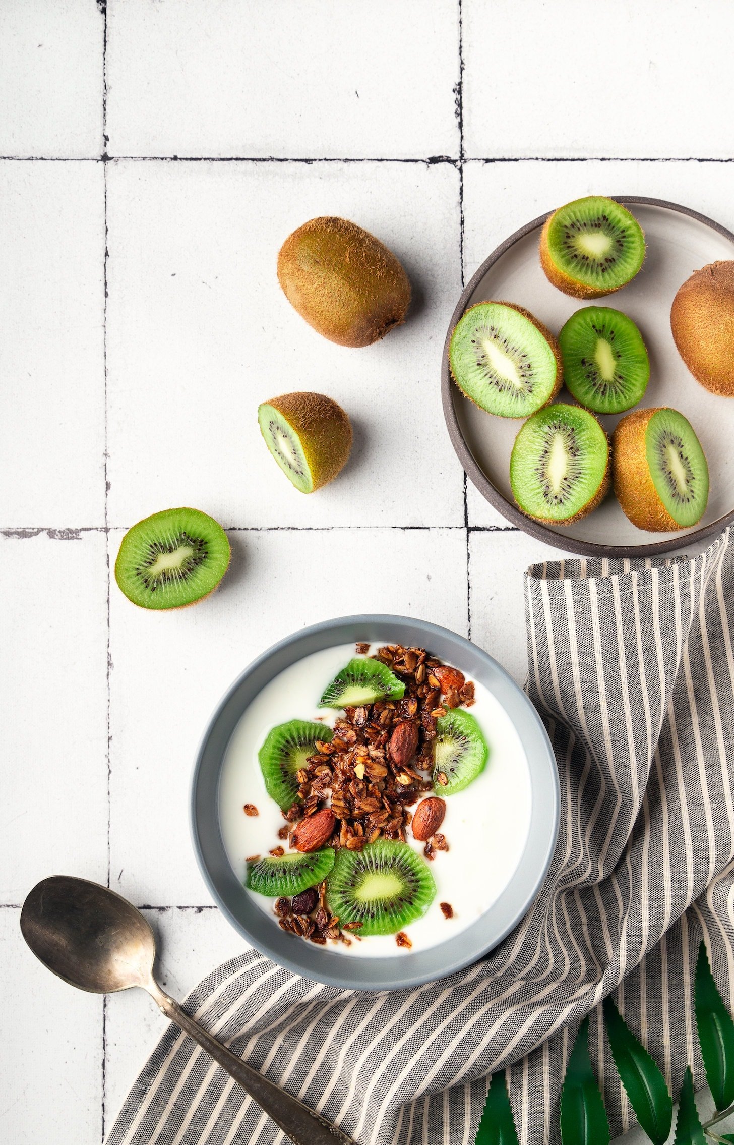 Homemade granola, muesli with kiwi fruit and yogurt on white tile background. Healthy breakfast bowl. Top view.