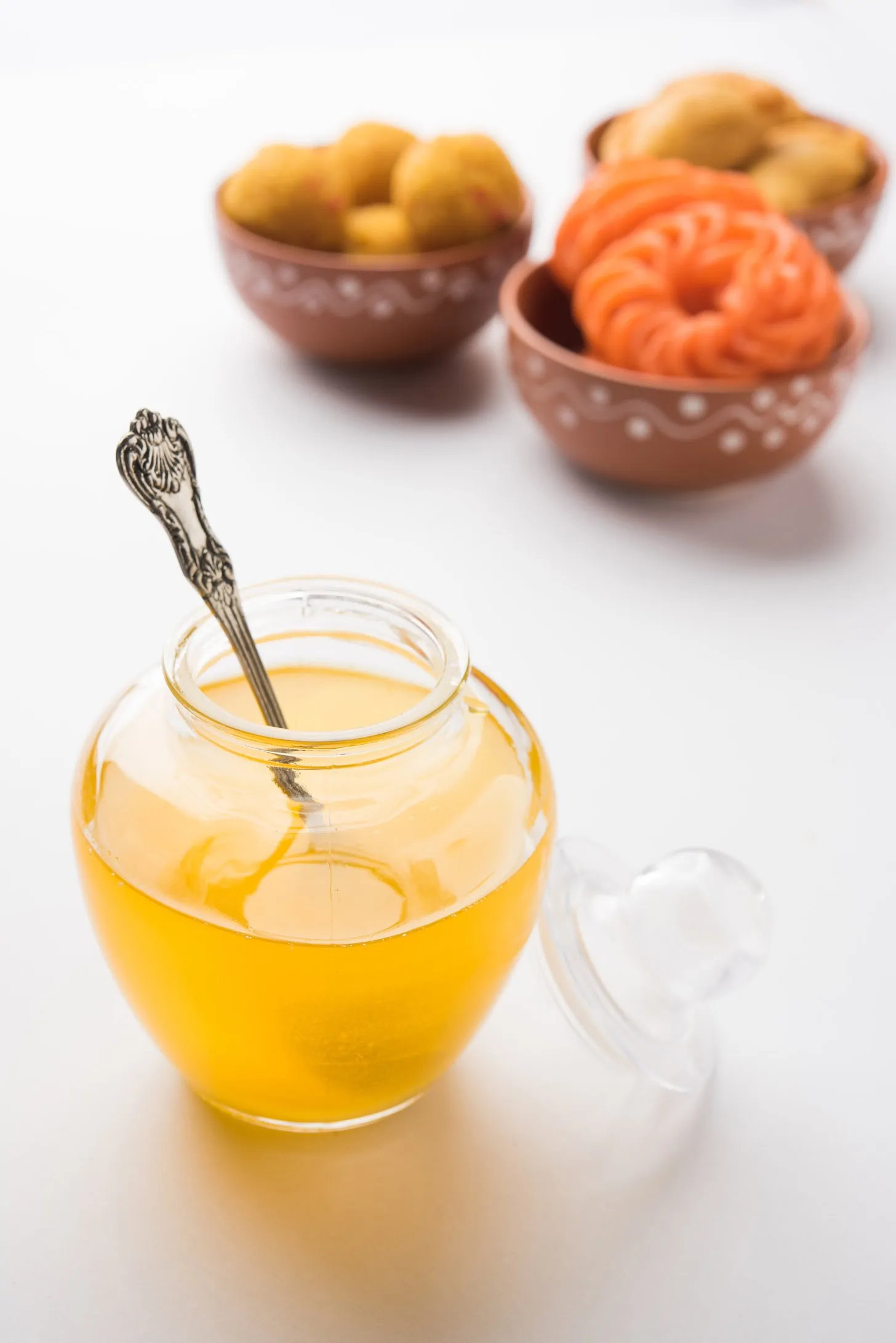 a jar of melted ghee with bowls of traditional Indian sweets in the background.