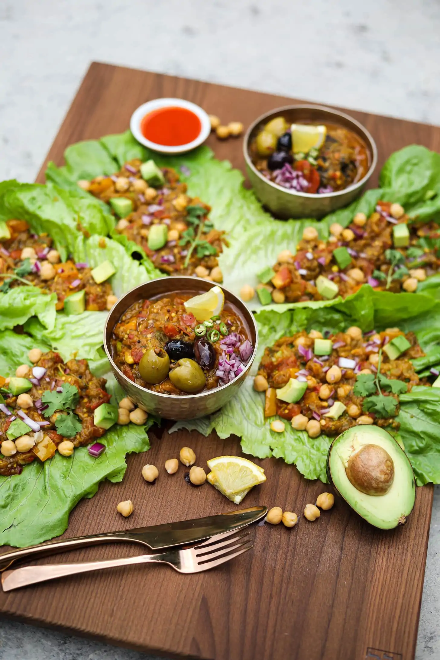 perspective image of two bowls of mashed eggplant surrounded by lettuce leaves stuffed with mashed eggplant topped with avocado pieces and chickpeas.