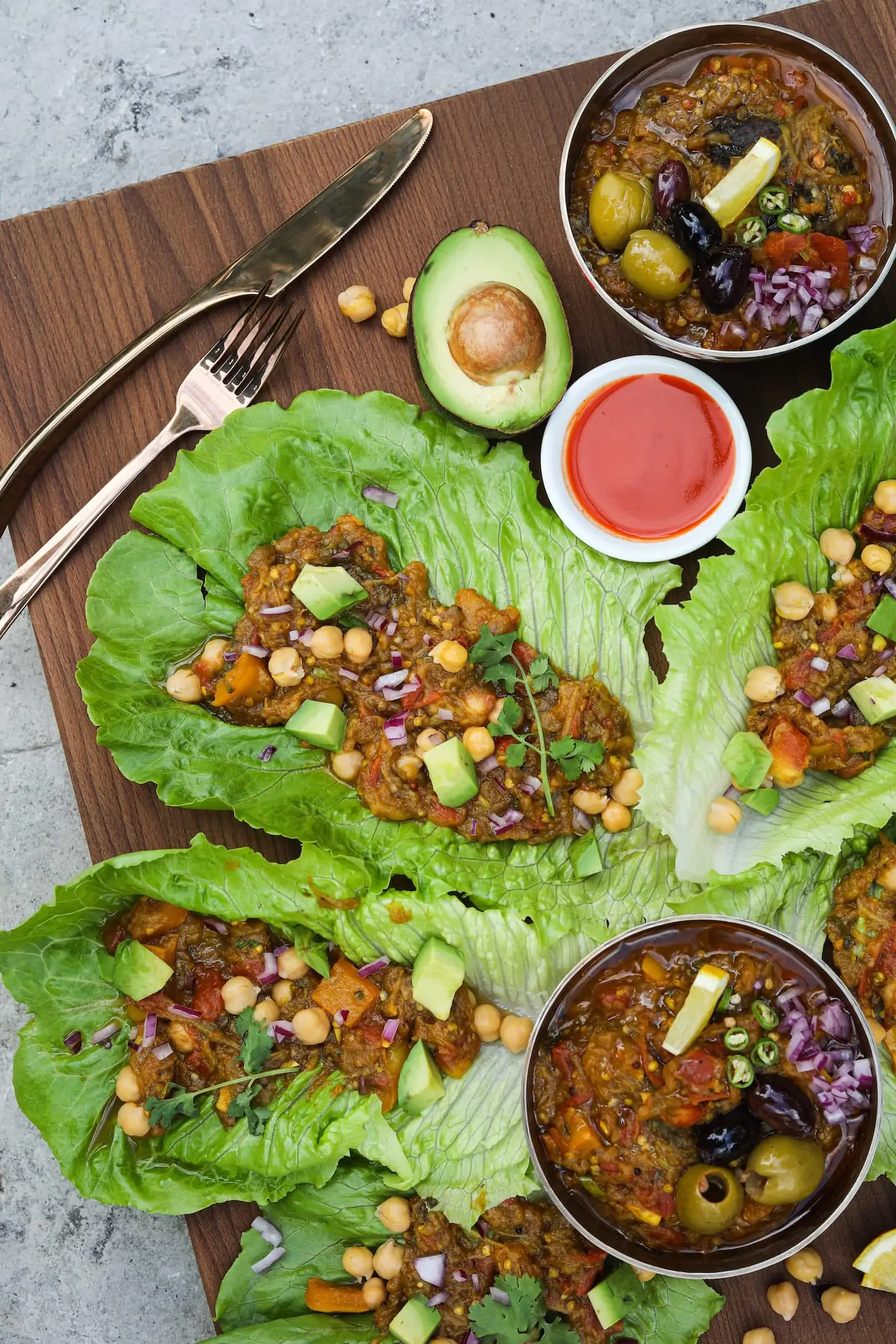 Flat lat of lettuce leaves stuffed with mashed eggplant and topped with avocado pieces and chickpeas with two bowls of mashed eggplant arranged around.