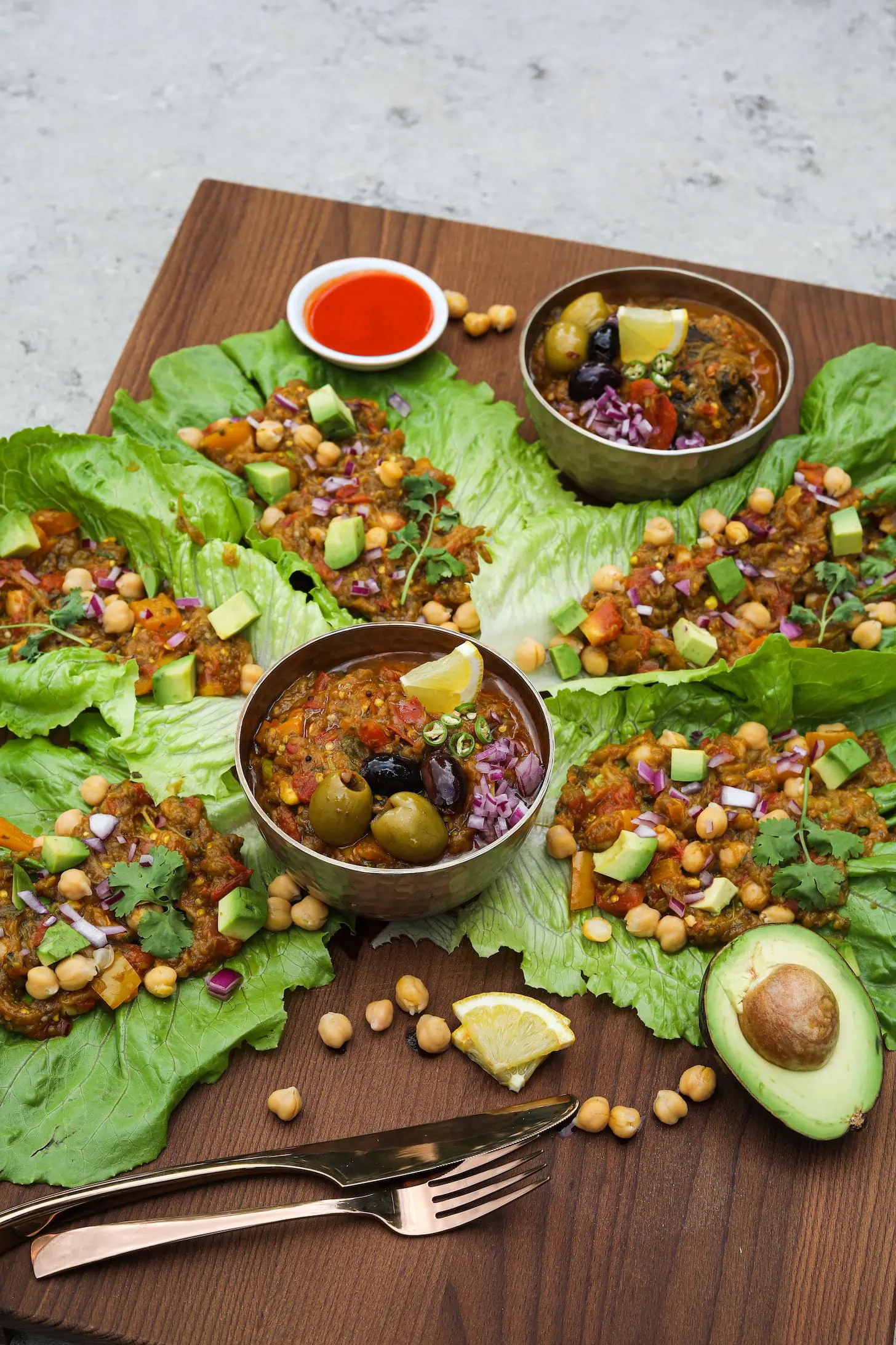 perspective shot of lettuce leaves stuffed with mashed eggplant and topped with avocado pieces and chickpeas with two bowls of mashed eggplant arranged around.