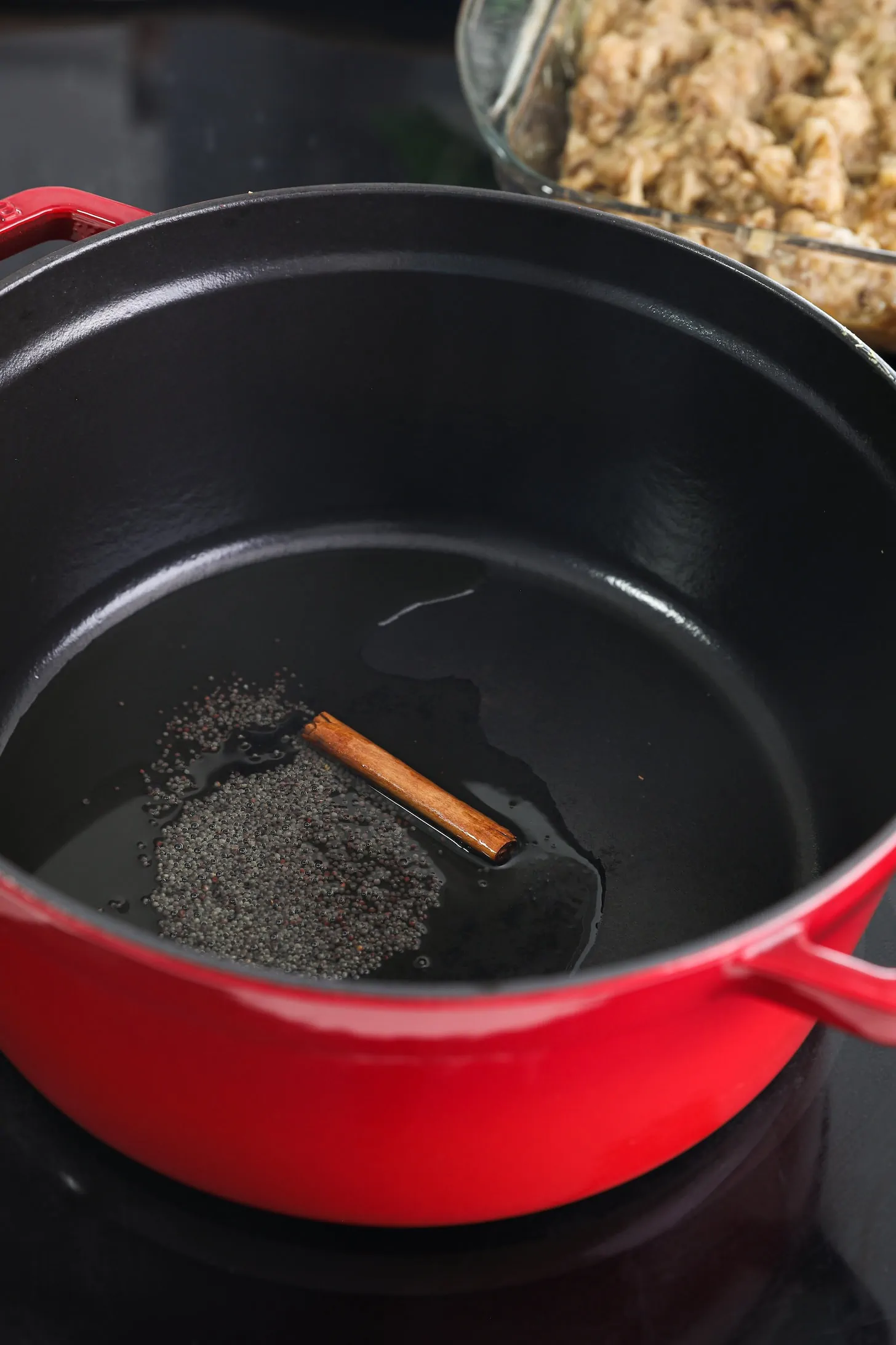 a red pot with oil, mustard seeds and a cinnamon stick.