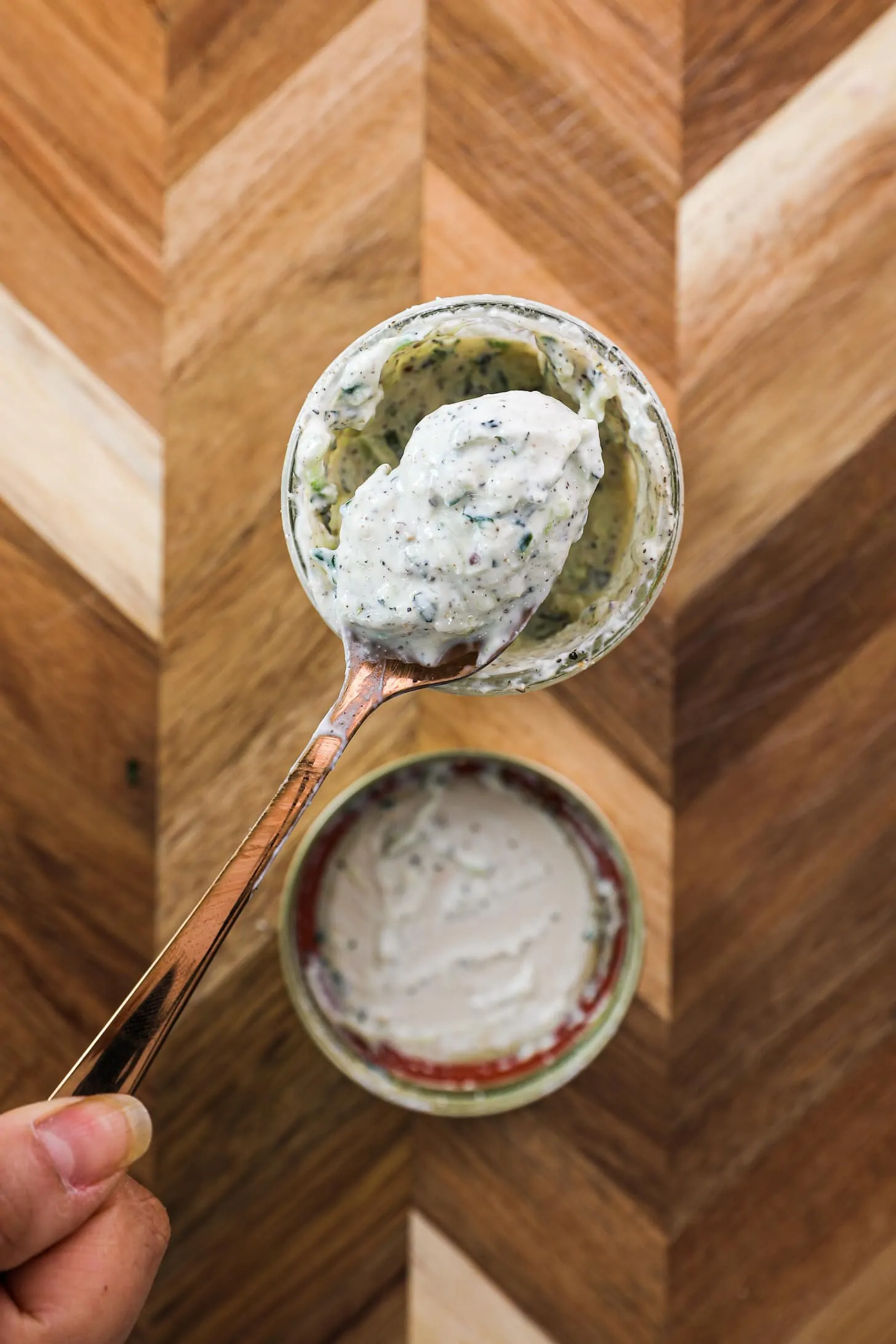 overhead image of a hand holding a spoonful of yogurt sauce, raita, over a mason jar.