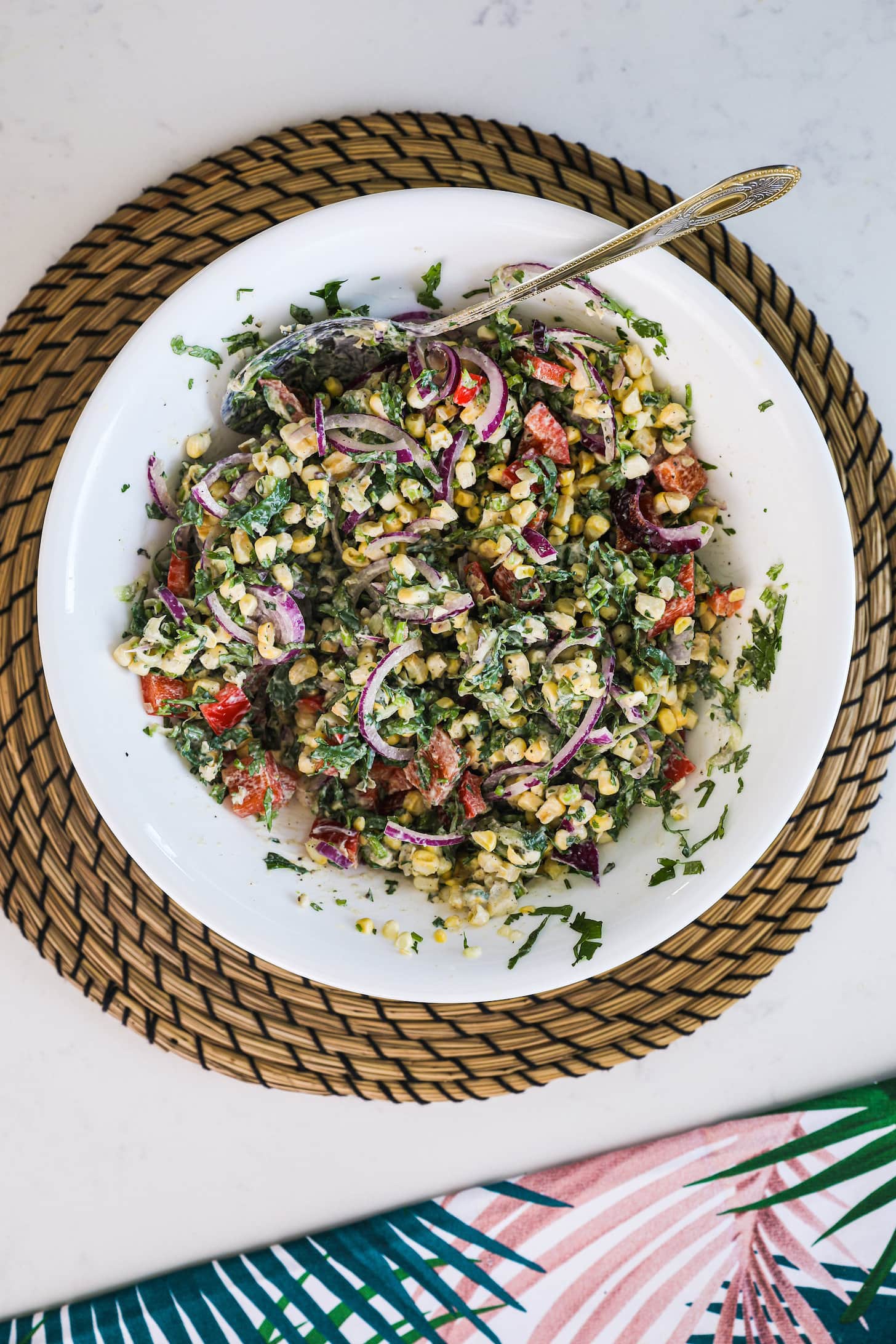 overhead image of a bowl of creamy salad made with corn, red onion, and greens.
