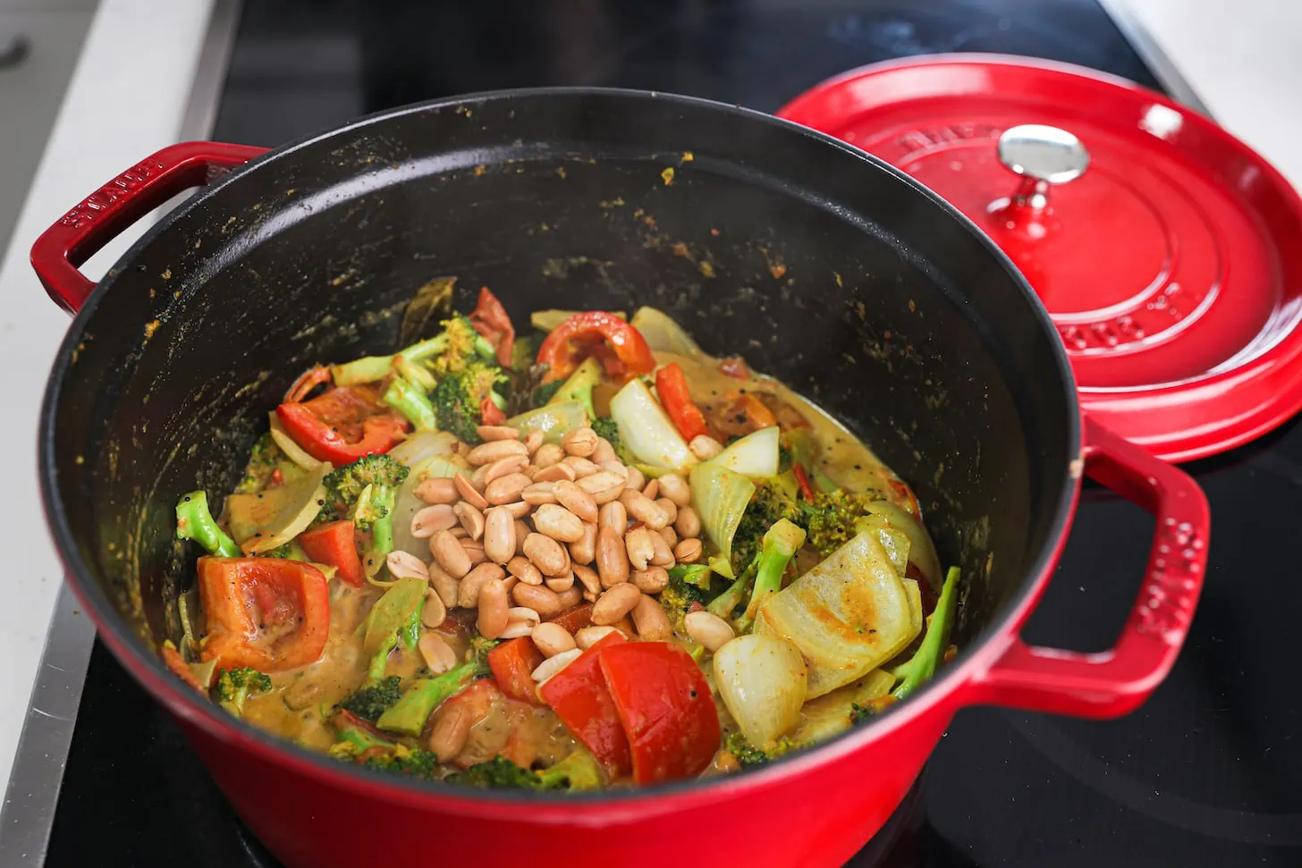 a red pot of cooked mixed vegetables topped with peanuts.