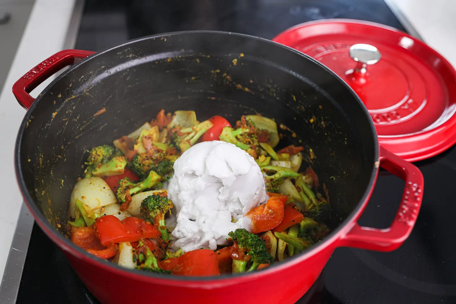 A red pot of cooked mixed vegetables with a large dollop of coconut cream.