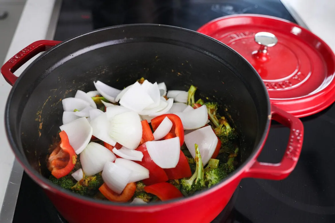 Slices of raw onion and red pepper in a cooking pot of broccoli.
