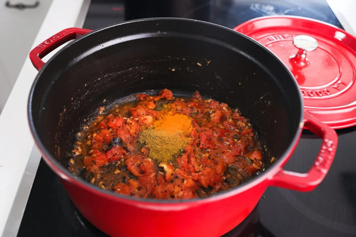 a red pot with red sauce topped with spices.