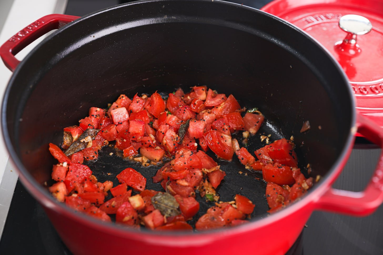 a red pot of chopped tomato with tiny black seeds and brown leaves.