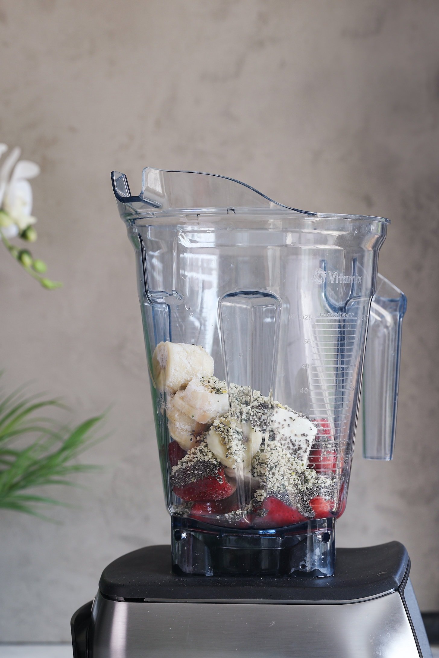 Perspective image of a blender with banana, berries and seeds in it.