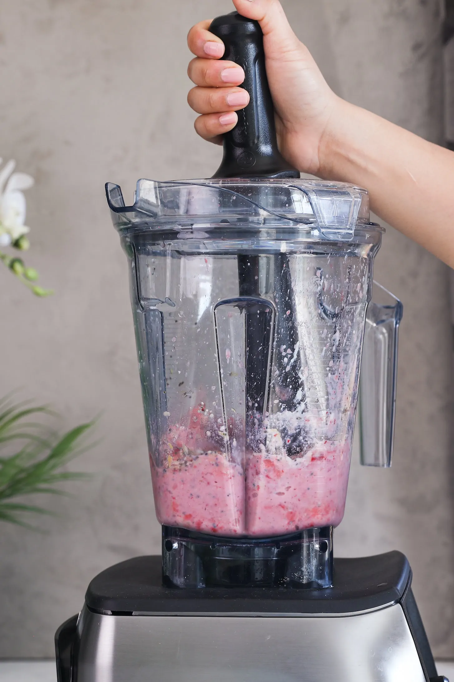 a hand holding a tamper stirring a pink mixture in a blender.