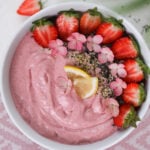 Overhead of a pink smoothie topped with strawberry halves, pink flowers and seeds.