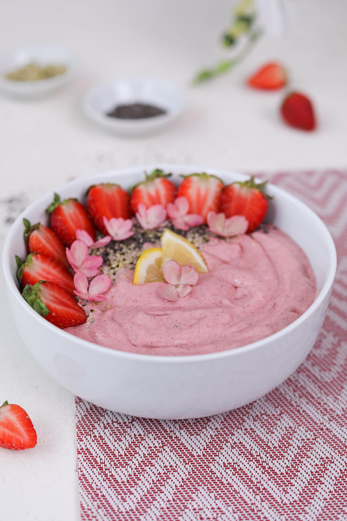 Perspective image of a pink smoothie topped with strawberry halves, lemon segments and pink flowers.
