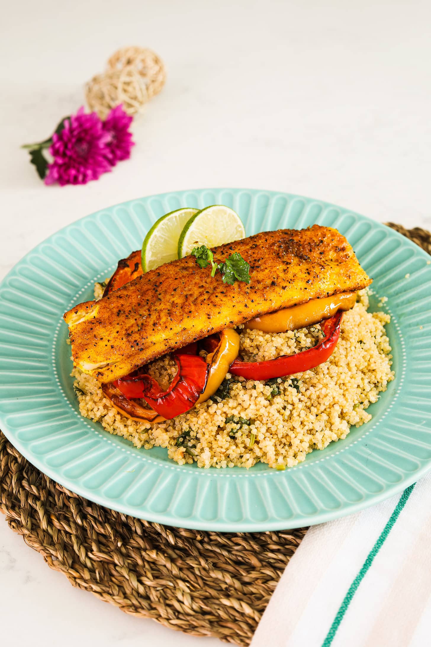 A plate of quinoa topped with roasted pepper rings, fish fillet and lime slices