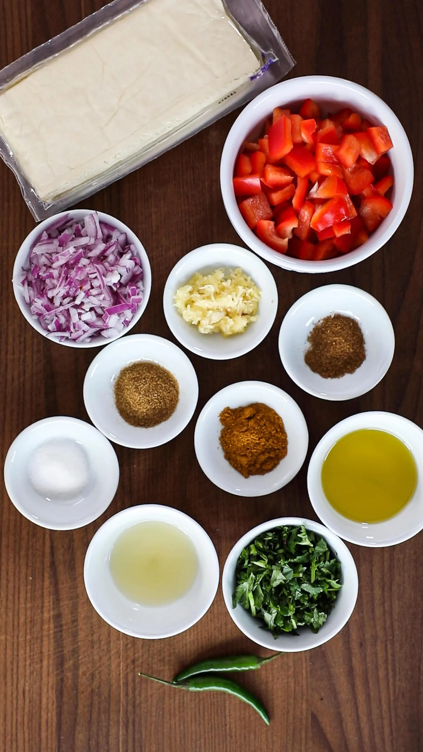 A selection of food ingredients (vegetables and spices) in ramekins on top of a wooden board.