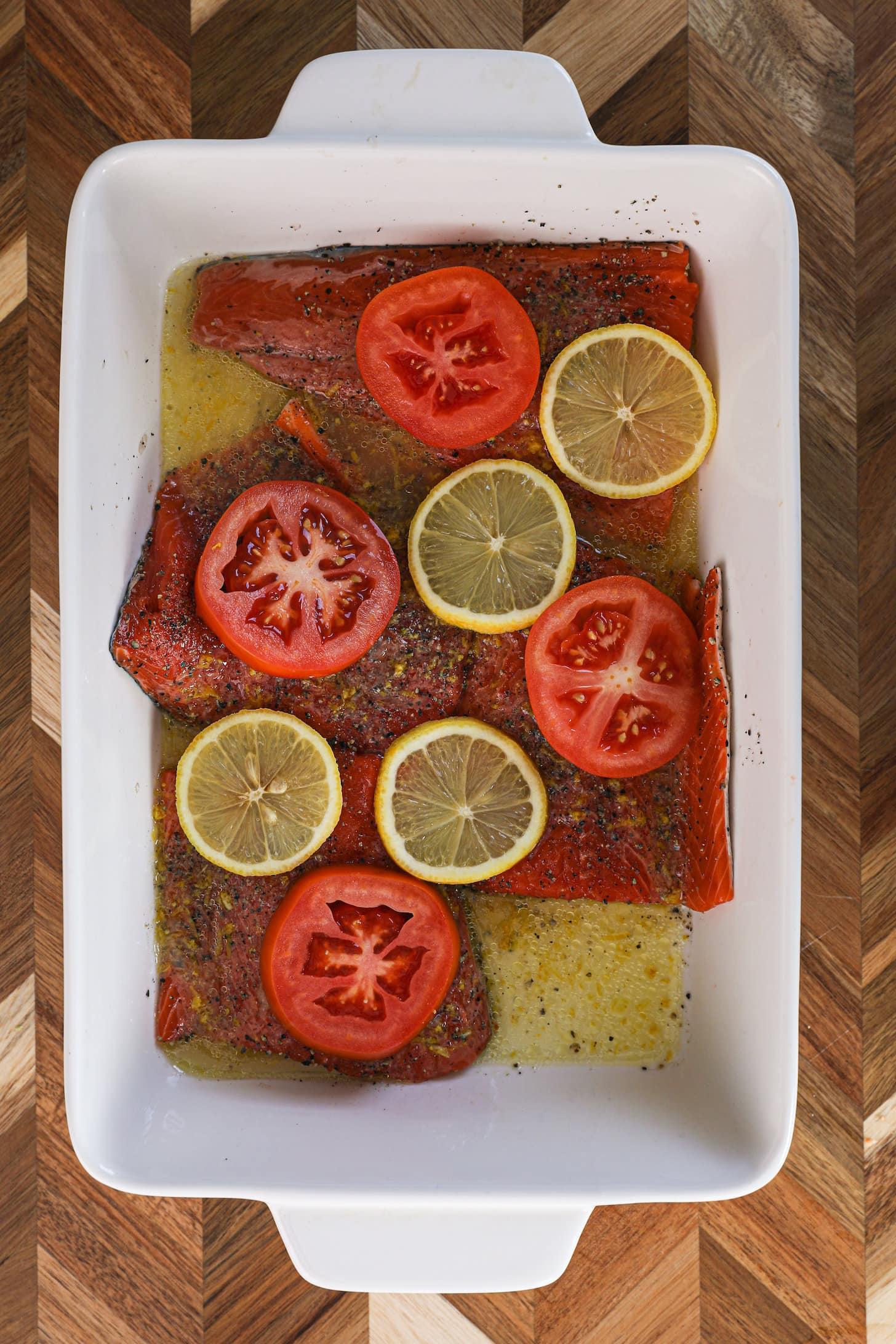 A white dish with fillets of salmon topped with lemon and tomato slices.
