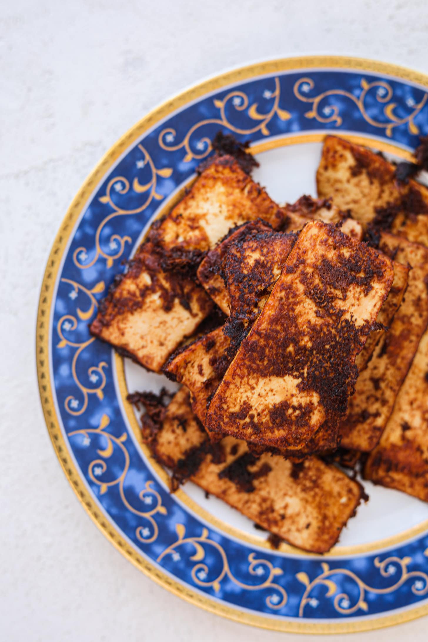 Overhead shot of a pile of crispy tofu slabs on a plate with a decorative blue boarder.