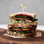 Two half tofu sandwiches stacked on top of one another, filled with salad and beetroot on a wooden board.