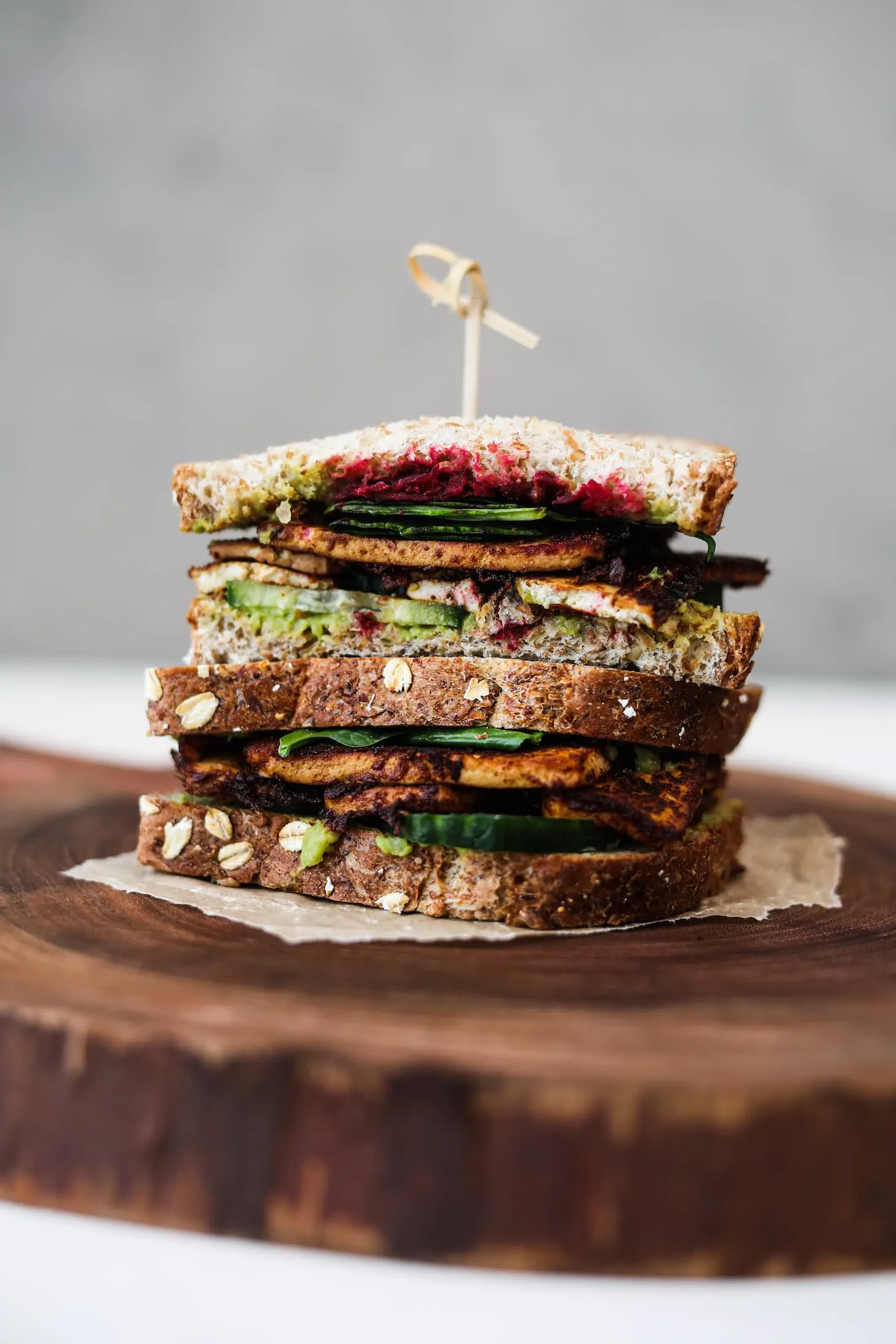 Two half tofu sandwiches stacked on top of one another, filled with salad and beetroot on a wooden board.