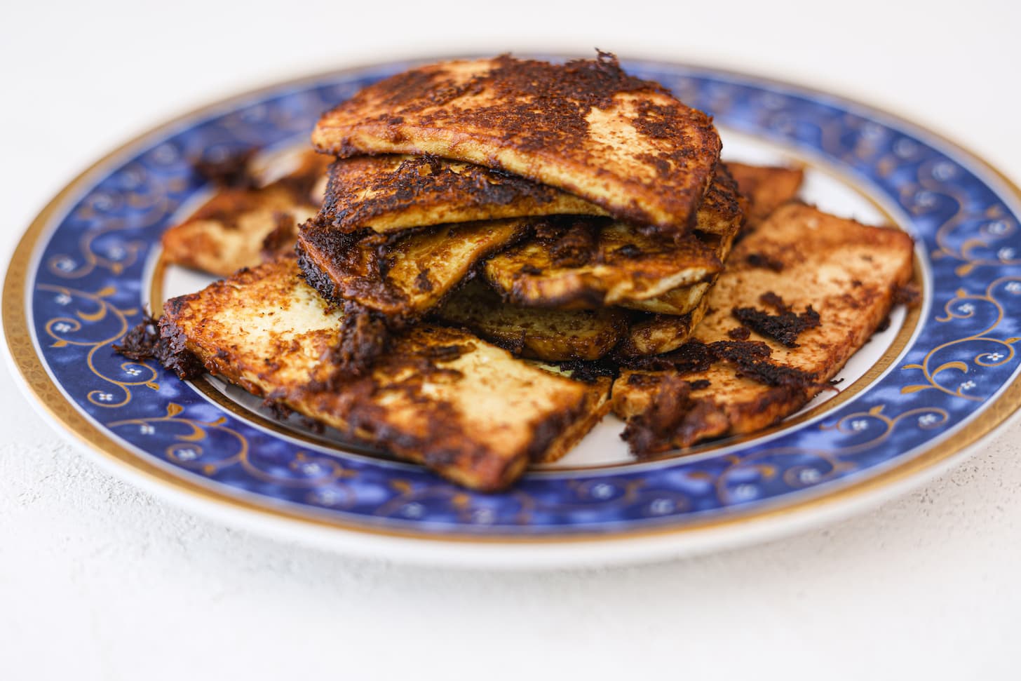 A plate with a pile of cooked slabs of tofu with a charred exterior.
