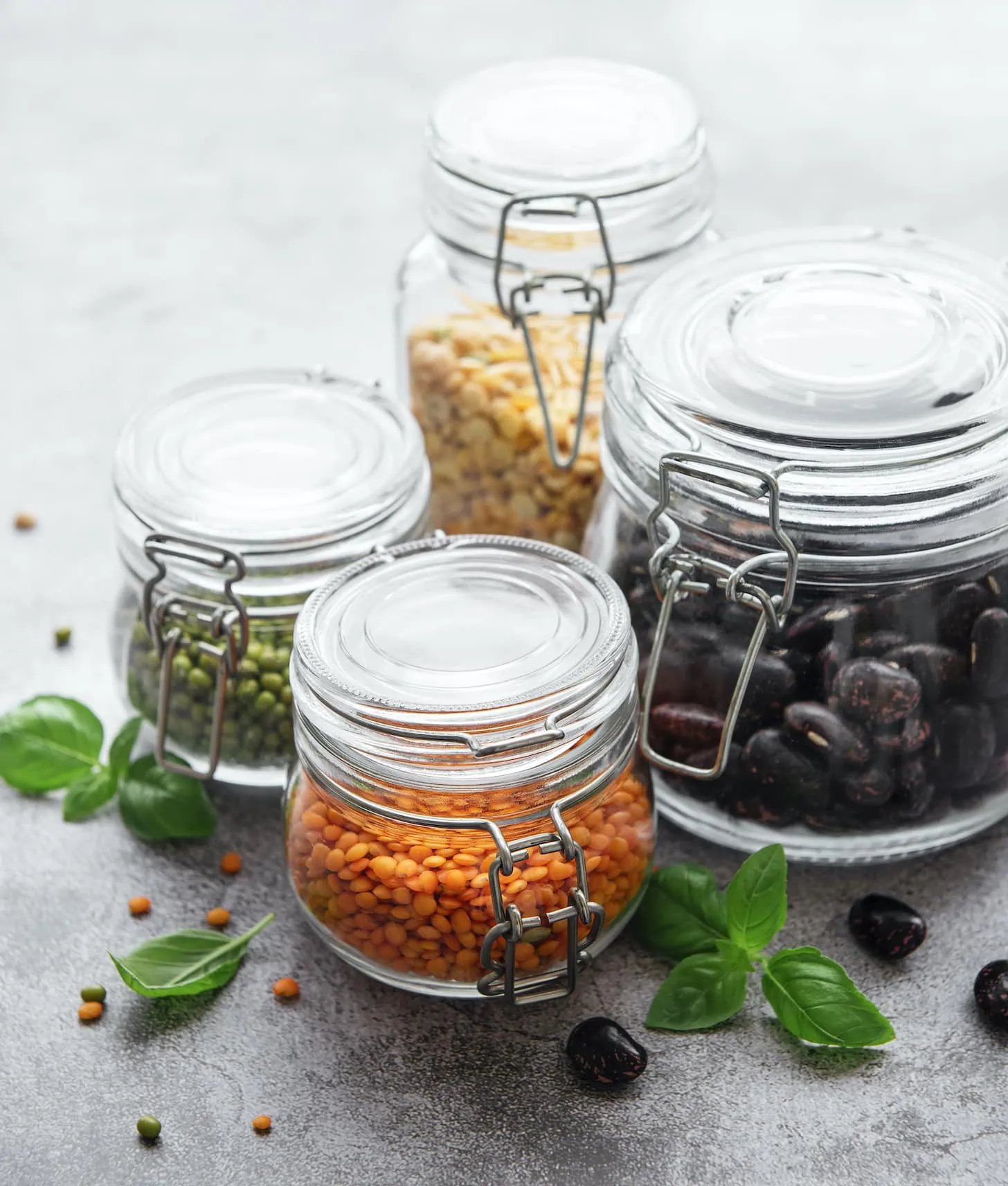 Glass jars with different types of legumes on a gray concrete background.
