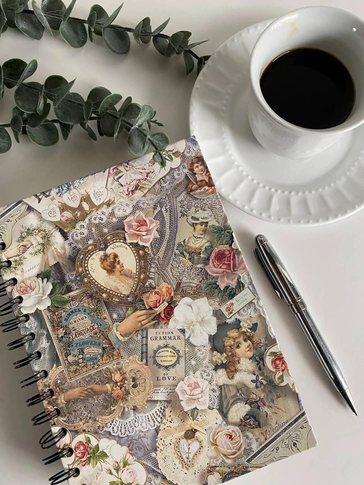 a floral journal with a pen, a cup of coffee and a plant close by.