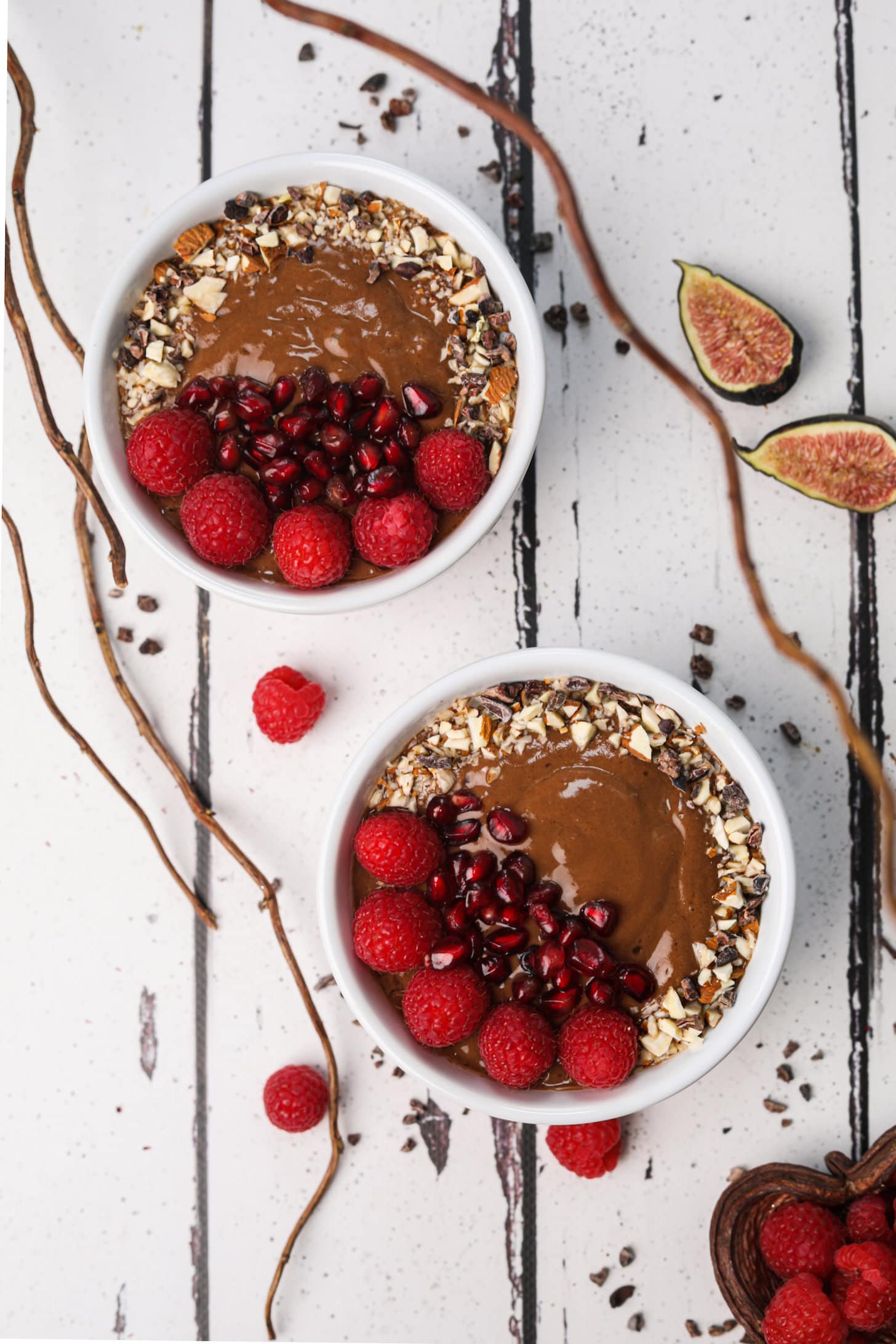 Flatlay image of 2 bowls of chocolate smoothie topped with berries, crushed nuts and pomegranate seeds.
