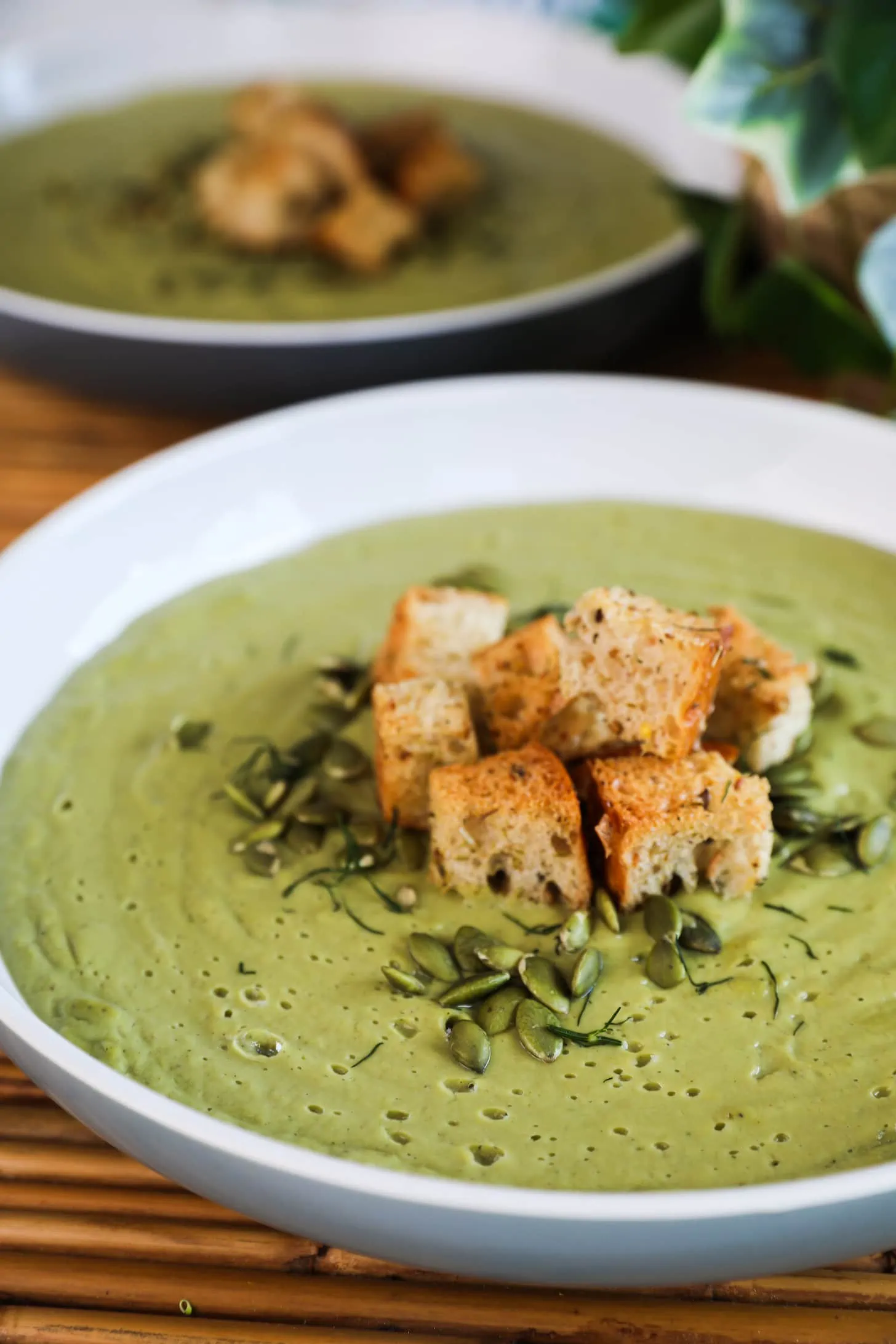 Angled image of green soup topped with croutons and seeds.