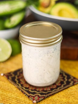 A mason jar with a white sauce in it on a decorative place mat.