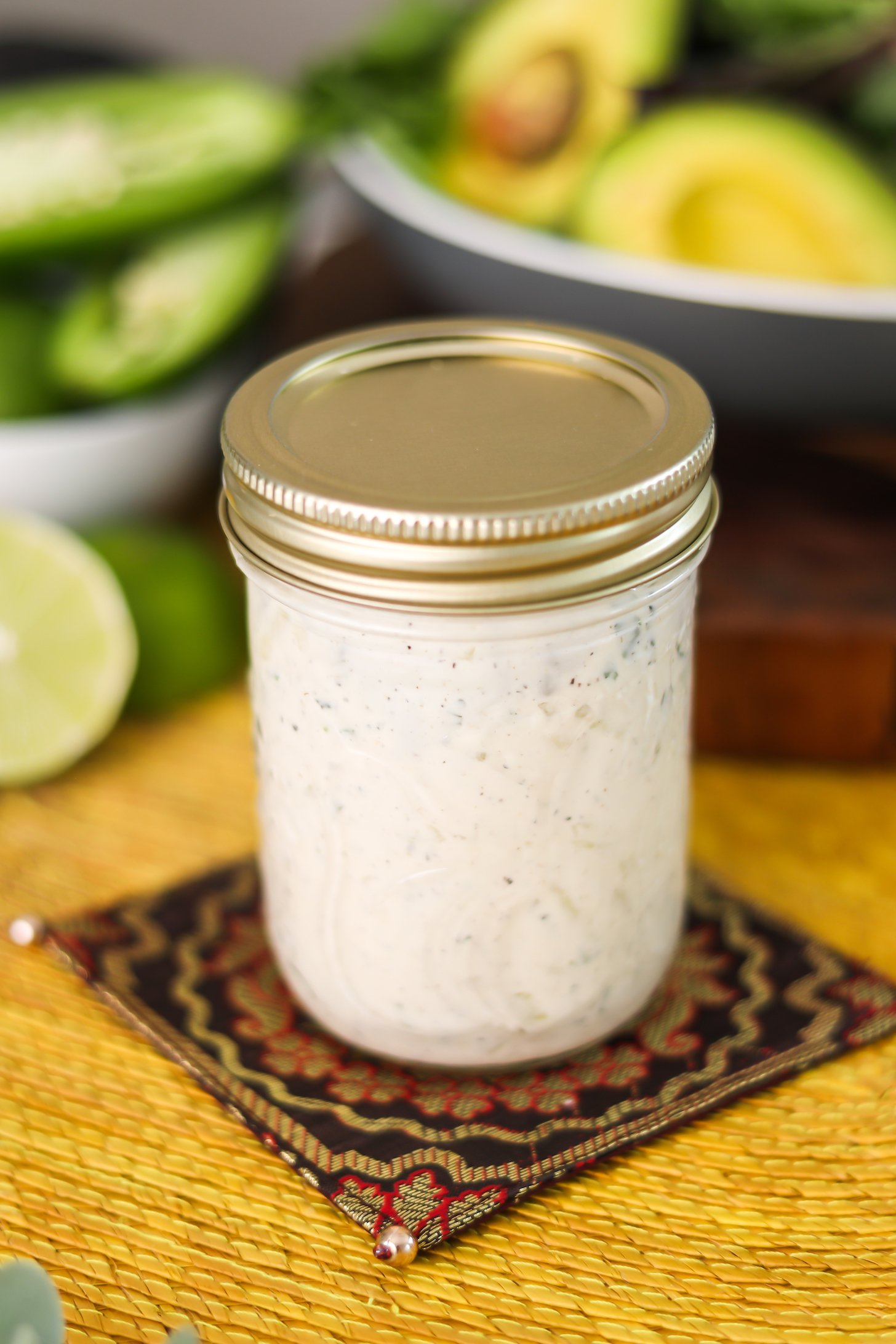 A mason jar with a white sauce in it on a decorative place mat.