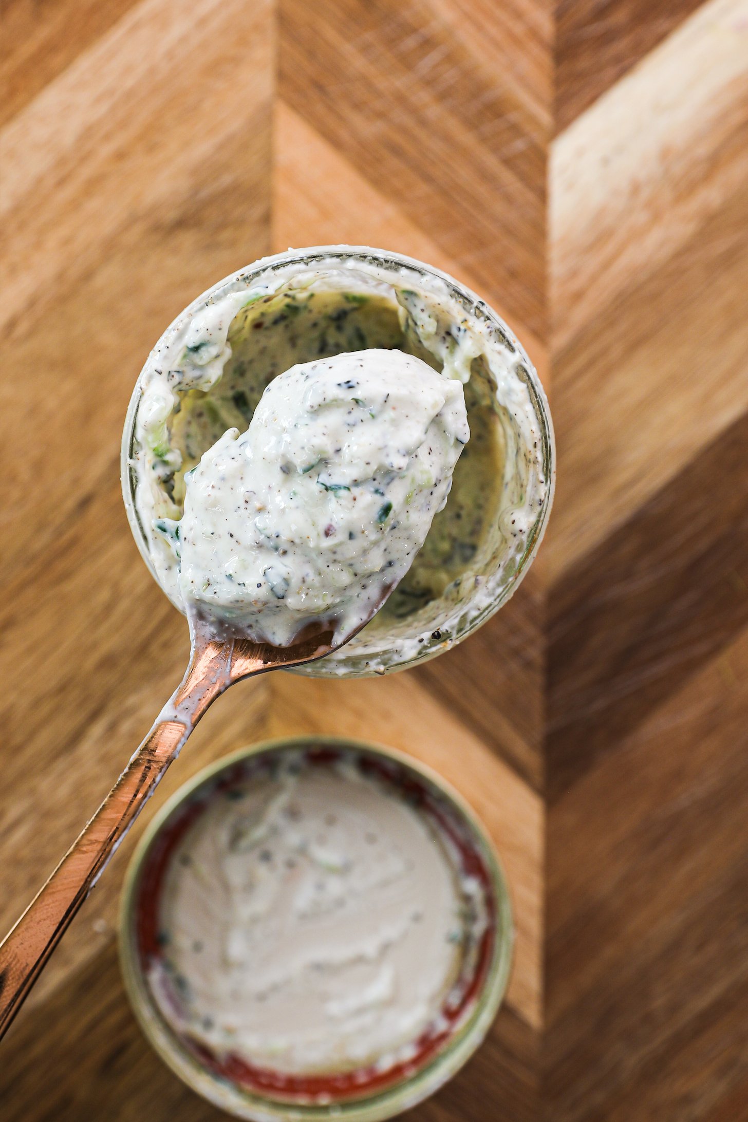 Top view of a gold spoonful of a yogurt sauce dotted with cucumber and spices.