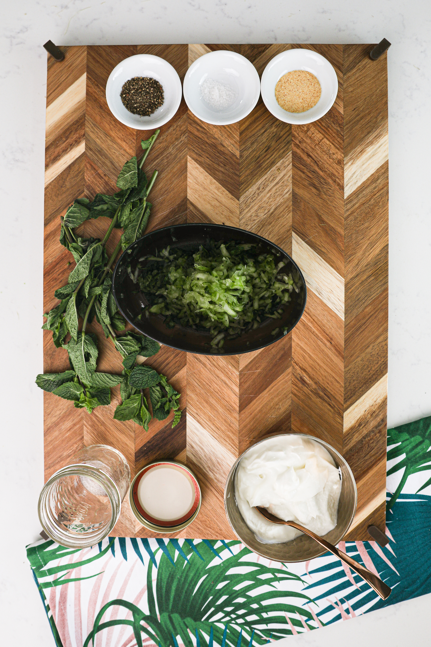 A display of food ingredients on a wooden board, including grated cucumber, spices and yogurt.