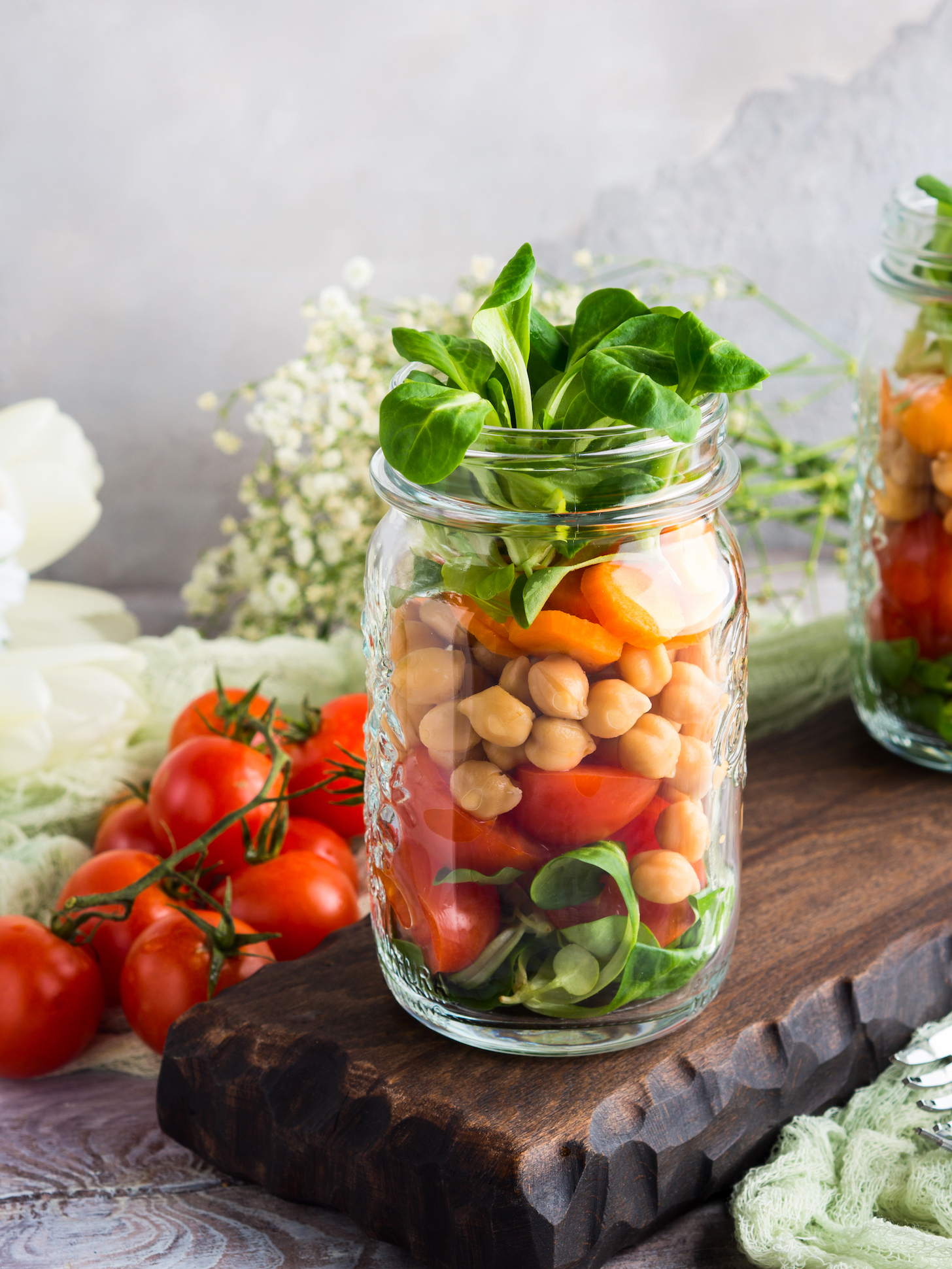 Fresh salad lunch with chickpeas, tomatoes, carrots and valerian served in mason jars.