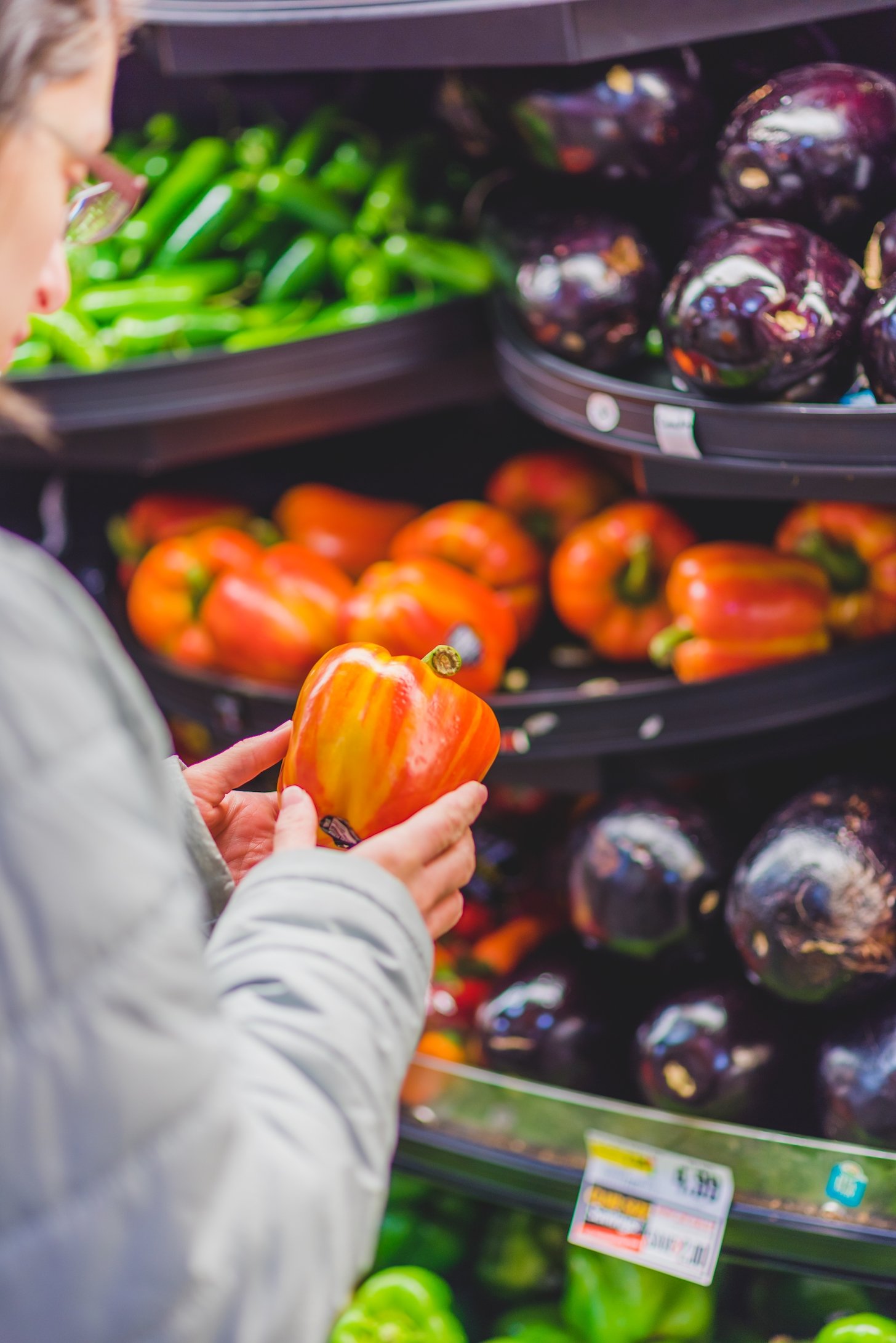 A person holding a pepper, while staring at it, in a grocery market.
