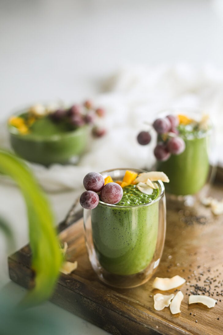 Perspective image of two glasses of a green shake topped with grapes.