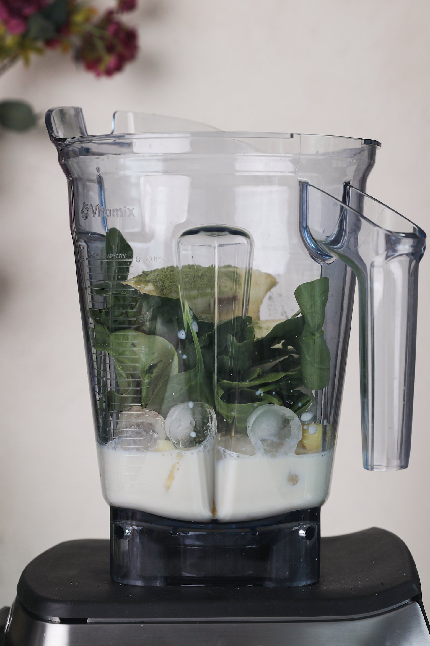 Perspective image of a blender filled with leafy greens, ice cubes, milk and a green powder.
