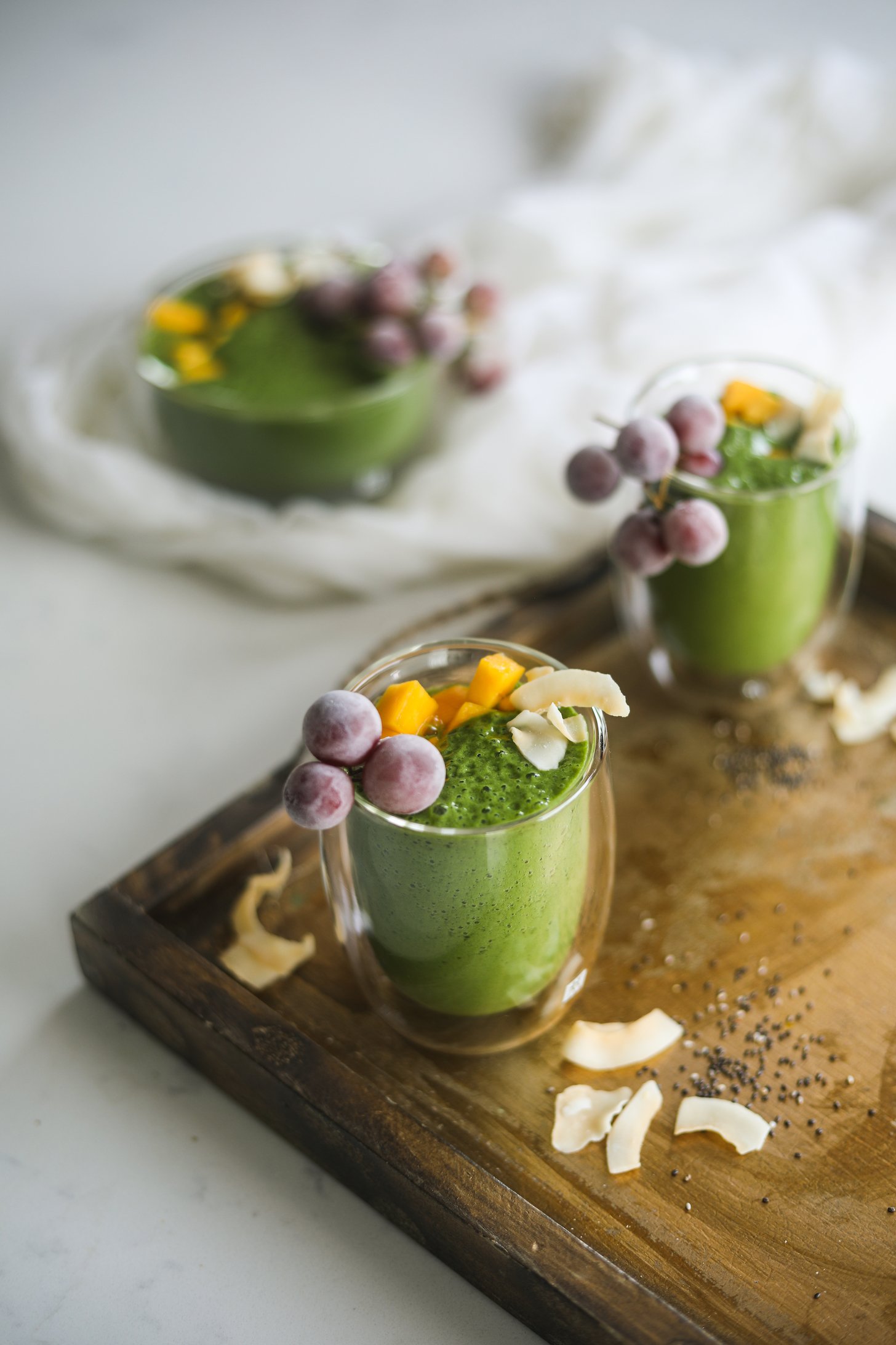 Overhead angled image of glasses of a green shake topped with grapes and mango chunks.