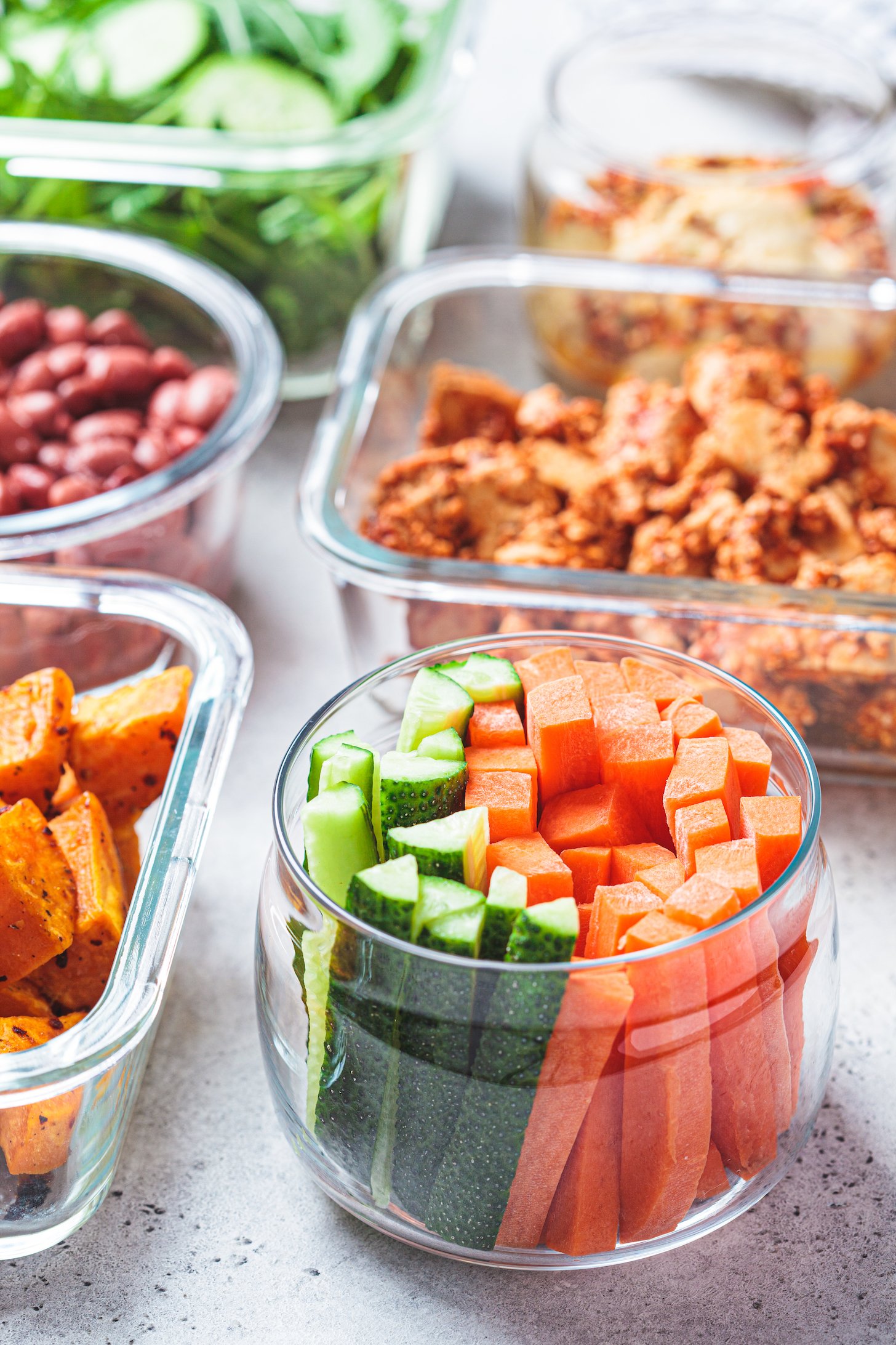 Vegan meal prep containers with cooked ingredients: marinated tofu, beans, baked vegetables, green salad and vegetable sticks.